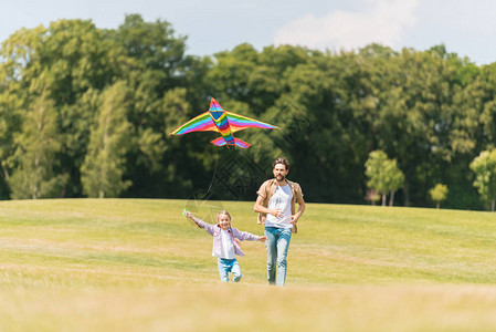 快乐的父女在草地上奔跑玩风筝图片