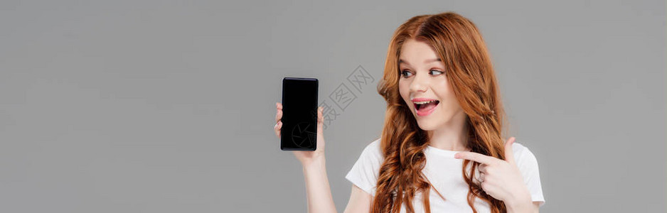 美丽兴奋的红发女孩用手指对着智能手机图片
