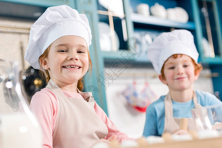 穿着厨帽和围裙的可爱孩子在厨房一起做饭时图片
