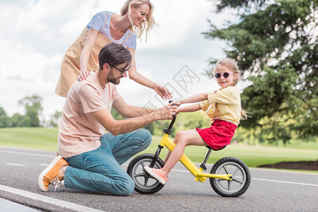 快乐的父母看着女儿在公园骑自行图片