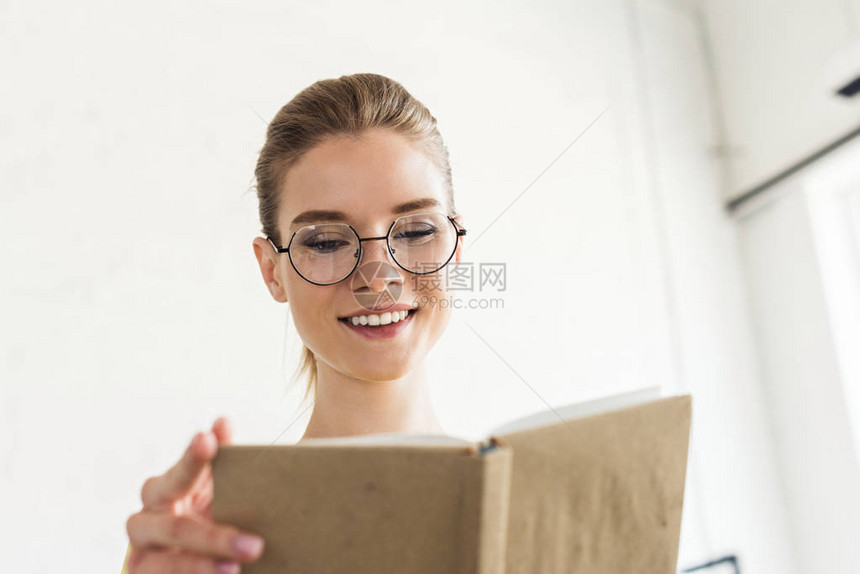 在阅读书中的眼镜中年轻微笑的女士图片