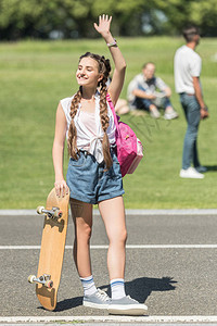带着滑板和背包的笑少女手挥图片