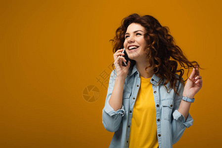 快乐的卷发红女人在智能手机上说话和触摸图片