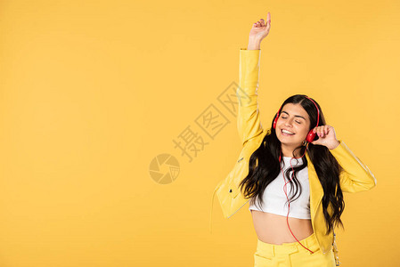 快乐的女孩跳舞用耳机监听音乐在黄背景图片
