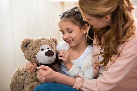 美丽的快乐母亲和女儿在家里玩泰迪熊游戏图片