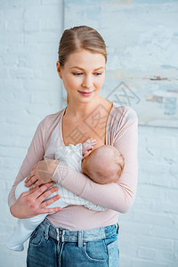年轻母亲在家中站立和哺乳婴儿时笑着微背景图片