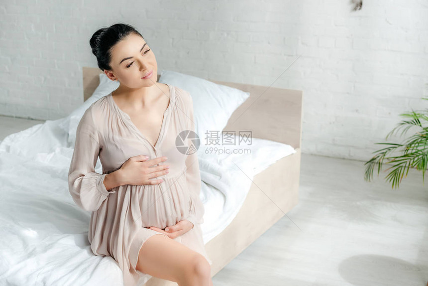 睡衣里梦幻的怀孕女孩坐在床图片