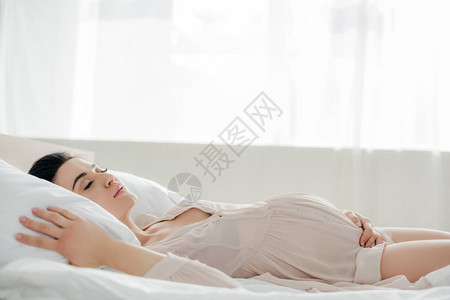 穿着睡衣的美丽的孕妇在床上睡图片