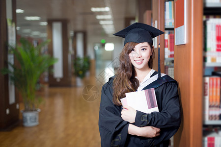 持有书籍和在图书馆穿著学术服饰图片