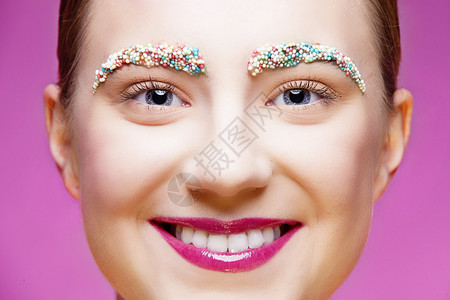 在眉毛上贴着多彩小糖果的微笑美丽的女孩图片