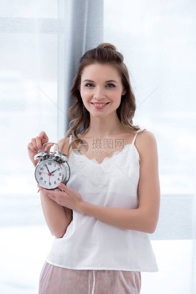 穿着睡衣的美丽的年轻快乐女人拿着闹钟图片