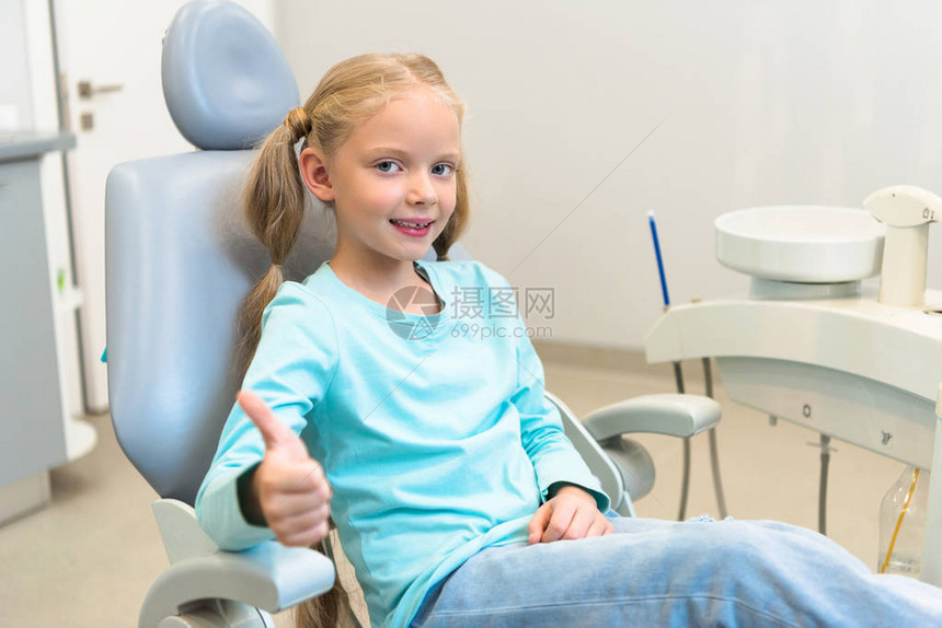 坐在牙医办公室的牙科椅上举起拇图片