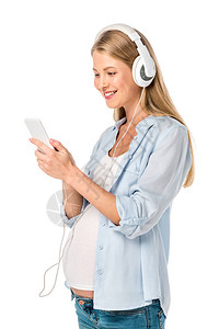 怀着快乐怀孕的妇用耳机和智能手机监听音乐图片