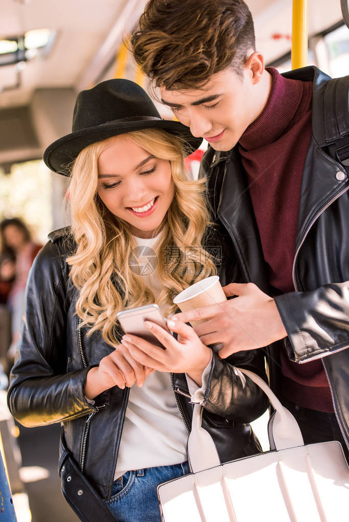 在公共交通中使用智能手机穿皮夹克的年轻夫妇笑图片