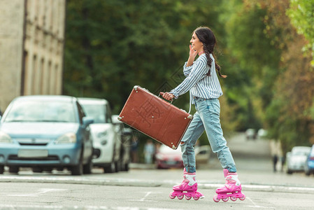 在街上拿着手提箱的溜冰滑雪鞋上的黑发美图片