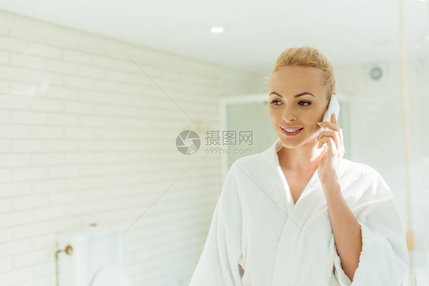 穿着浴袍的美丽笑着微笑的年轻女子在浴室里用图片