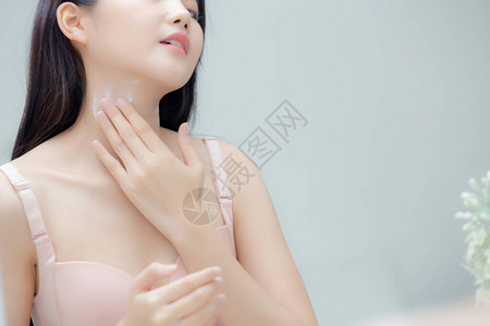 美丽感的年轻亚洲女照镜子在颈部和信息上涂抹奶油图片