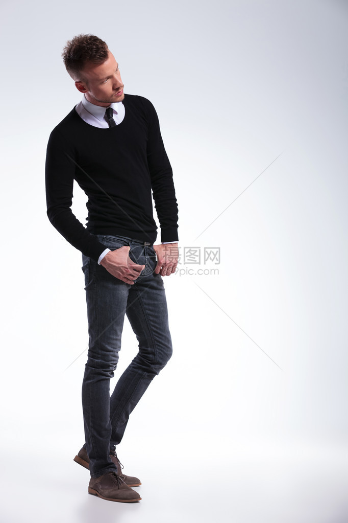 完整图片显示一名临时青年男子在口袋中用拇指站立时视而不见的全长照片在浅灰色图片