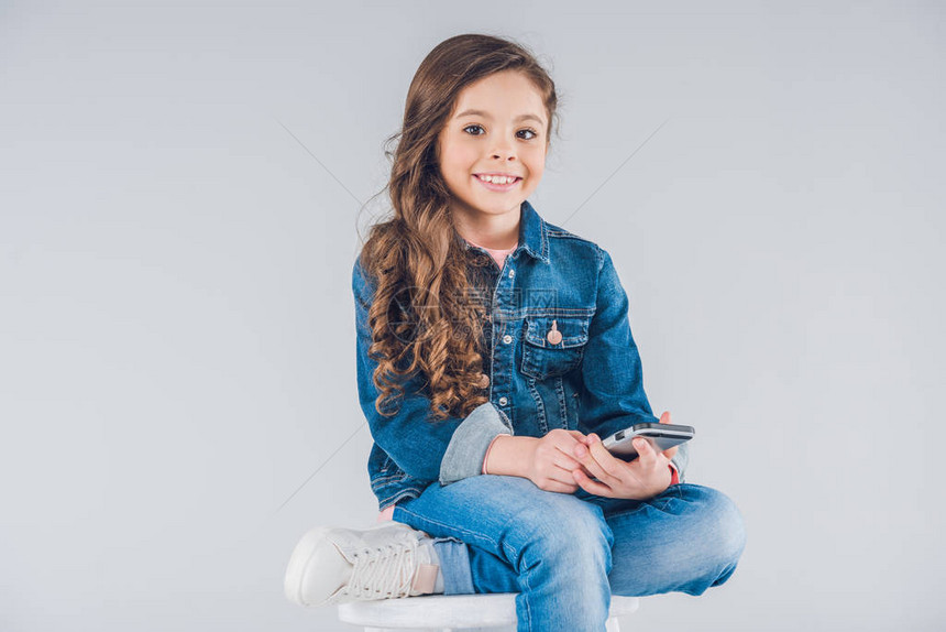 可爱的小女孩坐在凳子上时拿着智能手机图片