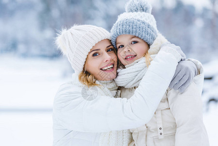 美丽的快乐母亲和女儿在冬季公园的相机上拥抱和微笑图片