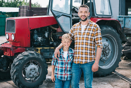身穿格斗衬衫的快乐父亲和儿子在农场站在一起时微笑着相机图片