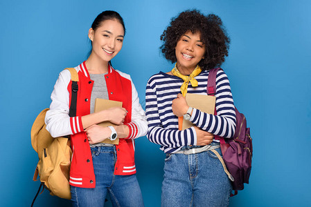 美裔和亚裔女学生装扮着书本在蓝图片