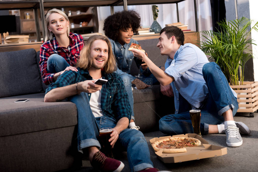 多元文化的朋友在家看电视和吃披萨图片