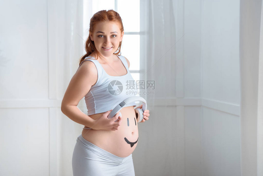 幸福的孕妇肚子上戴耳机家里戴着微笑符号的图片