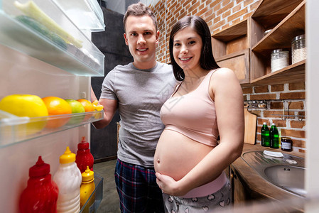 微笑着看厨房冰箱的年轻怀孕夫妇图片
