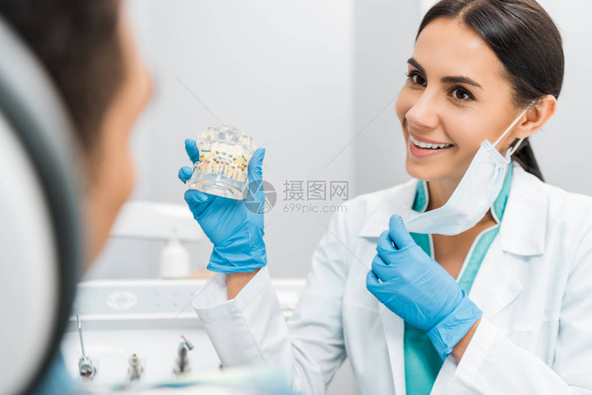 带着牙套给病人展示牙科下巴模型的微笑女图片