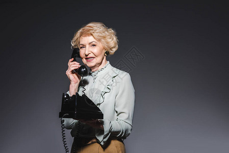 微笑着的老女人用古老的手机在黑图片