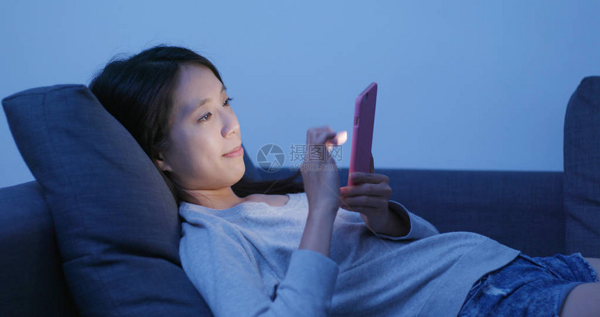 妇女使用移动电话晚上躺图片