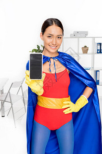 快乐美丽的亚洲超级英雄清洁工拿着带空白屏幕的智能手机图片
