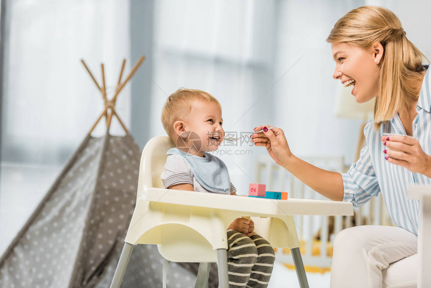 快乐的母亲喂养儿子在高椅子和婴儿食图片