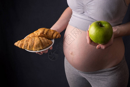 一个孕妇肚子里拿着一盘装着垃圾和健康食品的盘子孕期体重控制和饮图片