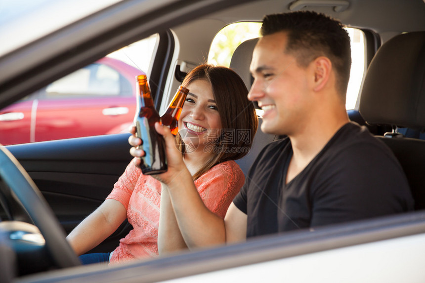 一对愉快的西班牙裔年轻成年人在开车时喝酒啤酒图片