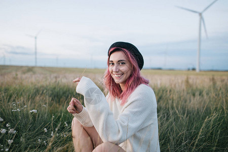 美丽的快乐女孩穿着白毛衣的粉色头发戴着帽子坐在田图片