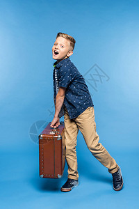 快乐的小男孩拿着手提箱看着蓝色的摄像头图片