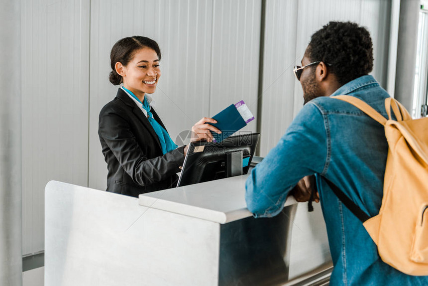 微笑的非洲裔美国机场工作人员给背着包的游客提图片