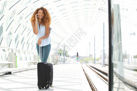 带着手机和袋子站在车站的年轻快乐女全身肖像图片