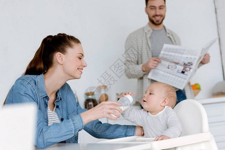 在厨房的婴儿瓶里装奶水喂着孩子父亲和报图片