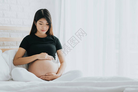 幸福的亚洲孕妇在卧室里抚摸肚子图片