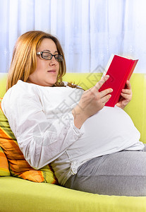 幸福的孕妇在家庭环境中阅读一本图片