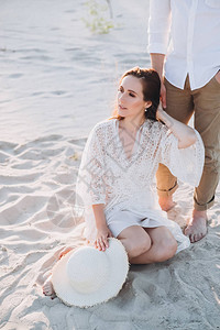 戴着帽子坐在海滩上并与男朋友握手的有魅力的女人图片