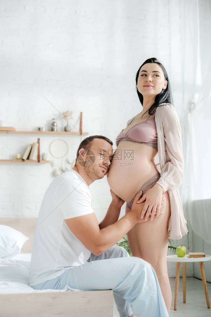 快乐的丈夫拥抱和倾听着他幸福的怀孕妻子图片
