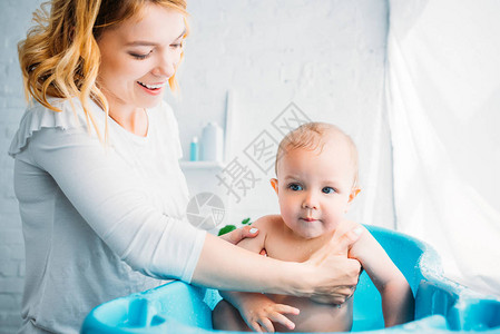 快乐的母亲在家里用塑料婴儿浴图片