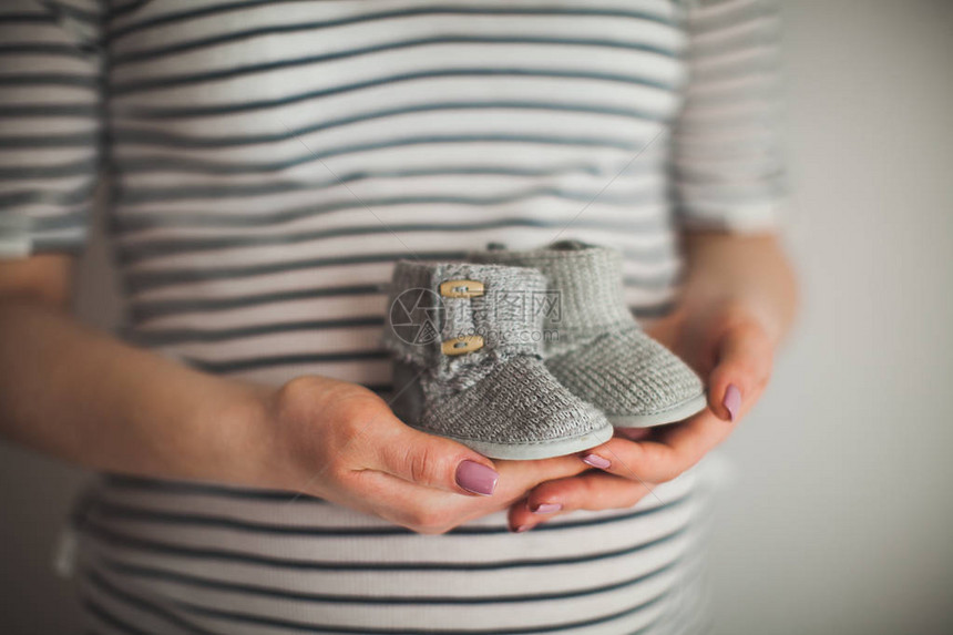 一只手拿着一双小鞋子这是灰色背景的婴儿鞋母婴主题怀孕图片
