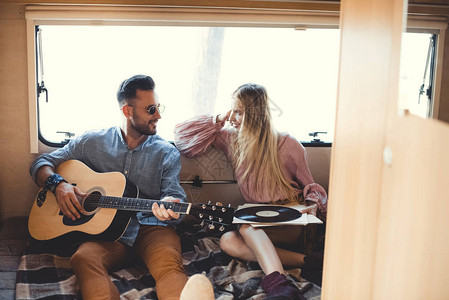 音乐家玩音响吉他而女孩看着他在野营车内持有图片
