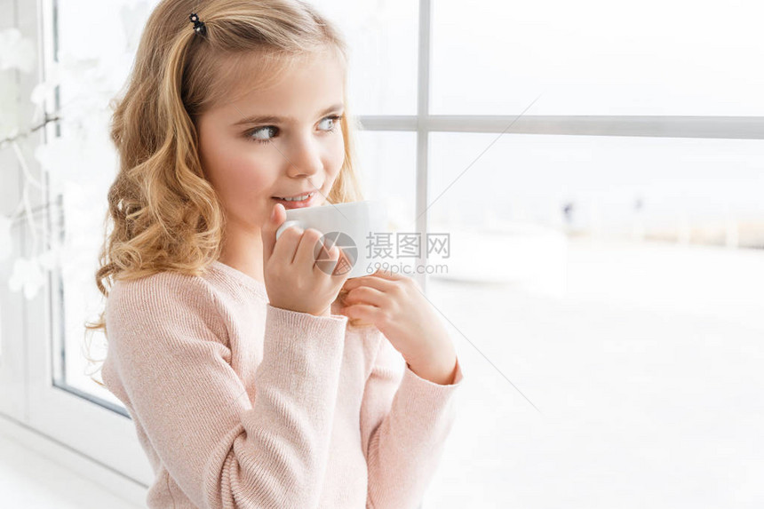 微笑的小孩喝茶透过窗户看图片