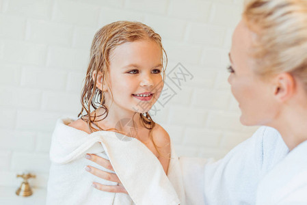 母亲在洗完澡后拿着毛巾和看可爱的快乐女儿时背景图片